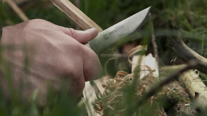 A person shaves a stick with a knife