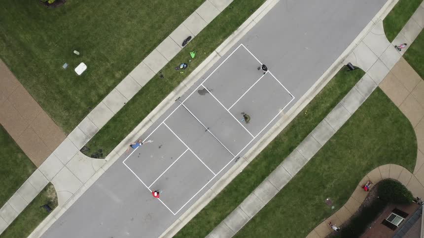 A birds eye view of people playing tennis and children on paths in a public park