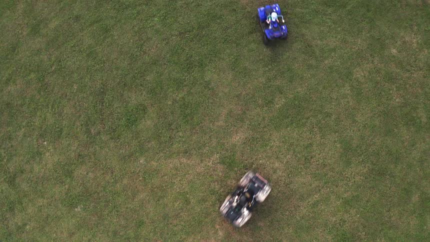 Two all terrain vehicles are traveling around in a grass covered field