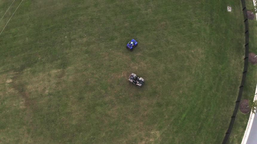 Two atvs driving circles on a grass lawn next to trees