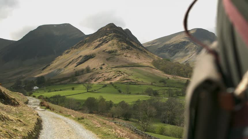 A gravel road leads to farmland and a mountain in the distance