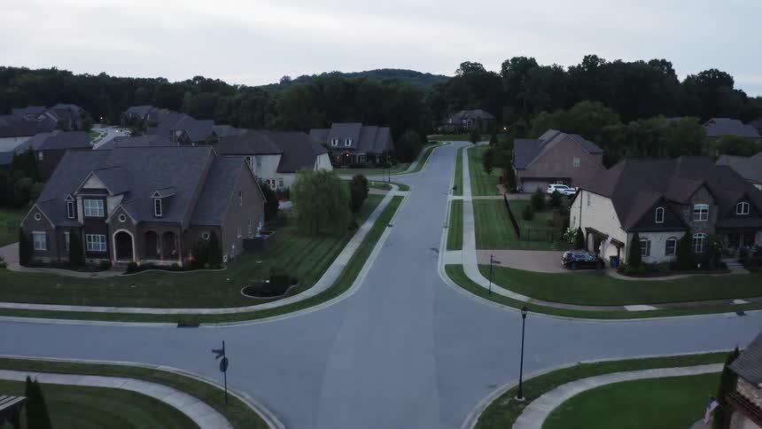 An aerial view of houses in a neighborhood with people walking outside and a vehicle driving down the street