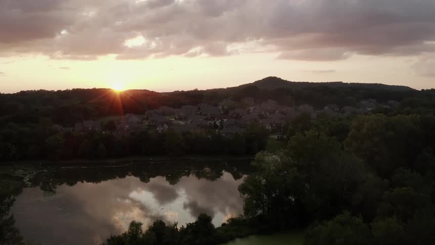 Sun rising in a cloudy sky over a forested mountain community with a lake