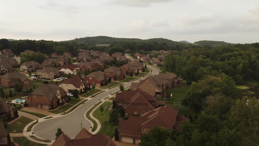 A neighborhood cul de sac surrounded by trees with a pond and hills on the horizon