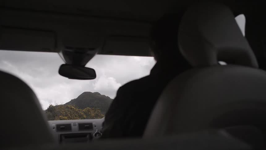 Two people riding in a car through mountainous area on a cloudy day