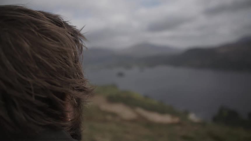 A man gazing at cloud-covered mountains near a lake