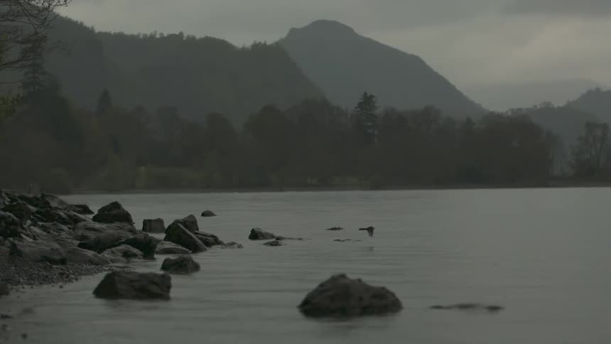 A bird is flying low over the water near some rocks