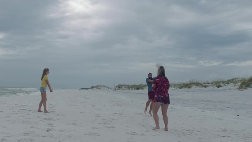 Father and mother playing with their teenage daugter with a volleyball on the white sand of a beach near the ocean