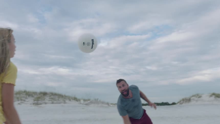 A man and two women on a beach playing with a ball with the sky and clouds in the background