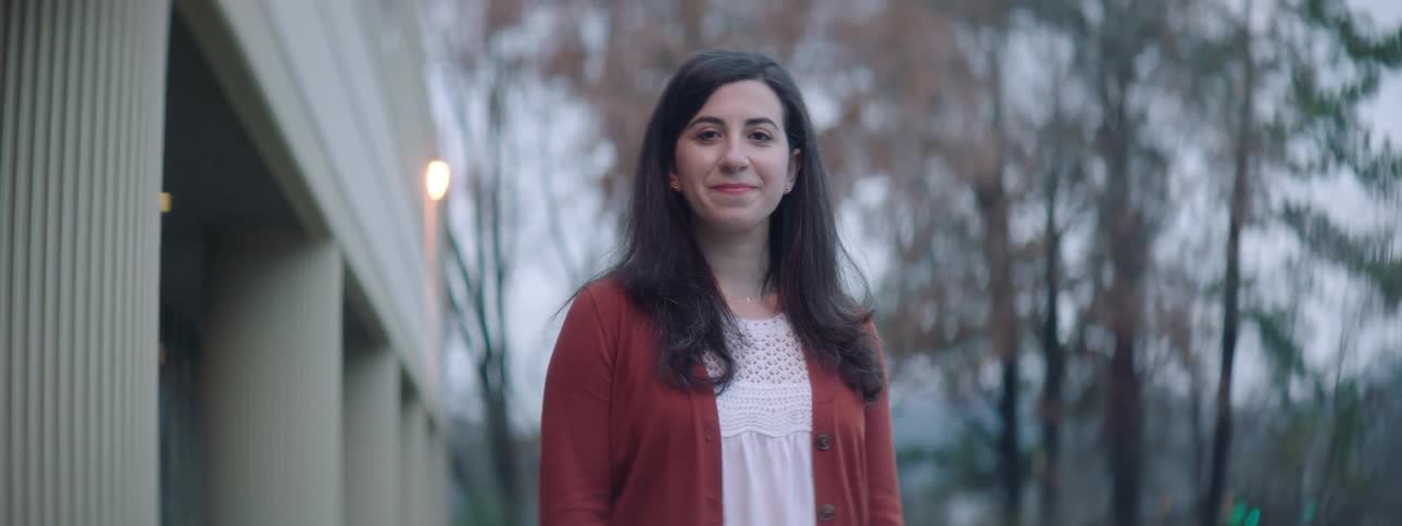 A woman standing outside turns her head and smiles proudly
