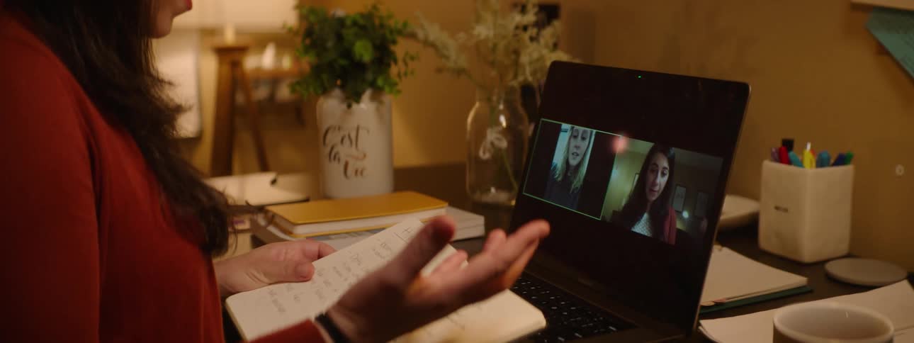 A woman at a desk with a laptop holding a book with a whiteboard in the background