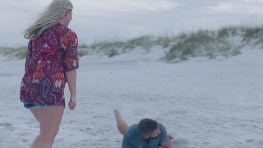 A man dives for a volleyball while playing with a woman on a beach