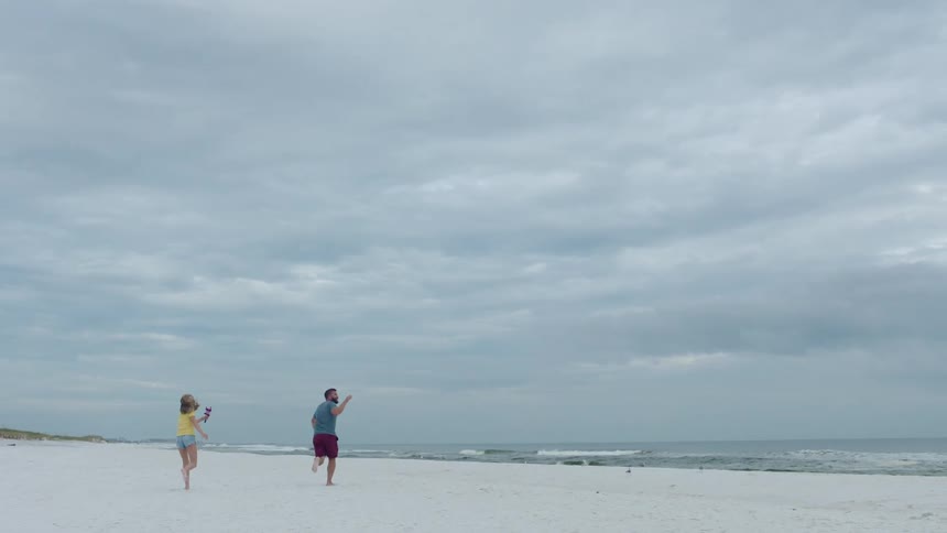 A man and a younger female run along the beach as the man holds the string of a kite