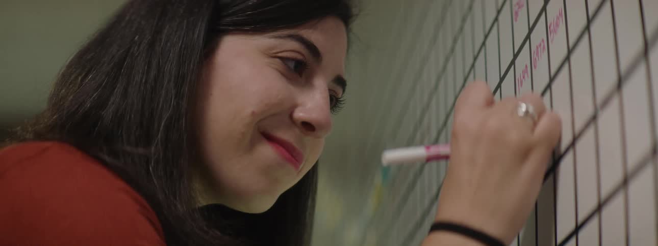 A woman in an office writes on a dry erase board