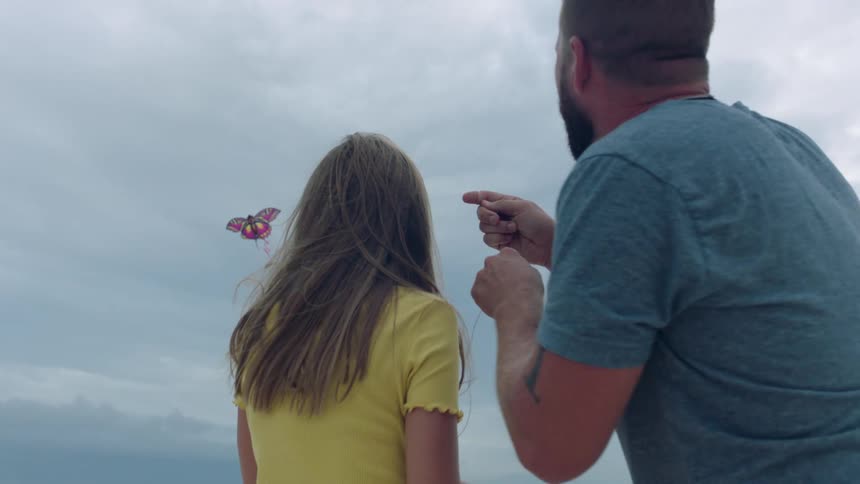 A man and a woman on a beach flying a kite with the sky and clouds in the background