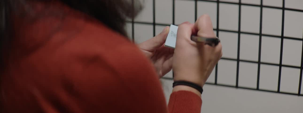 A woman in a room writing on a sticky pad with a pen