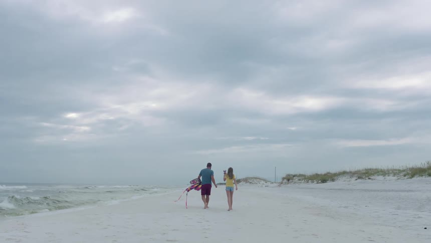 A father and daughter walking down the beach with a kite