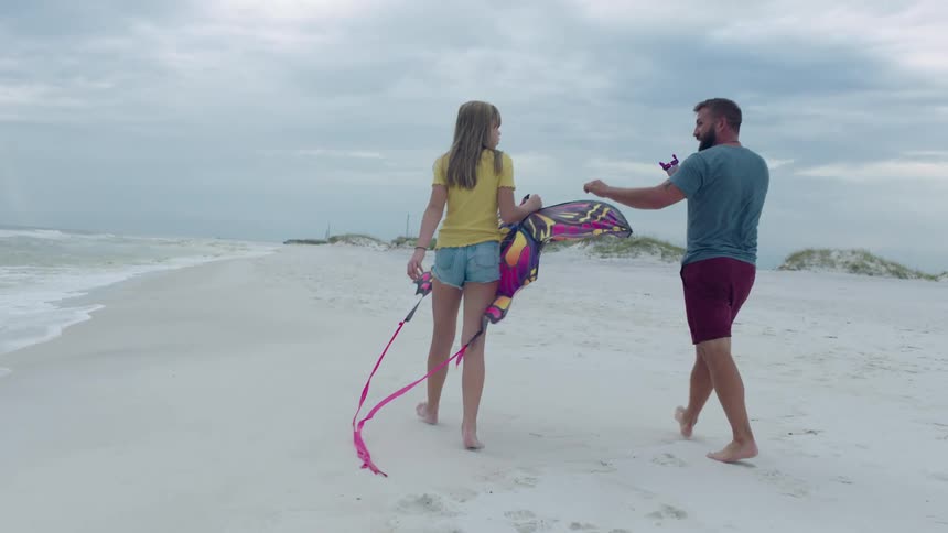 A man and woman walking down the beach with a kite