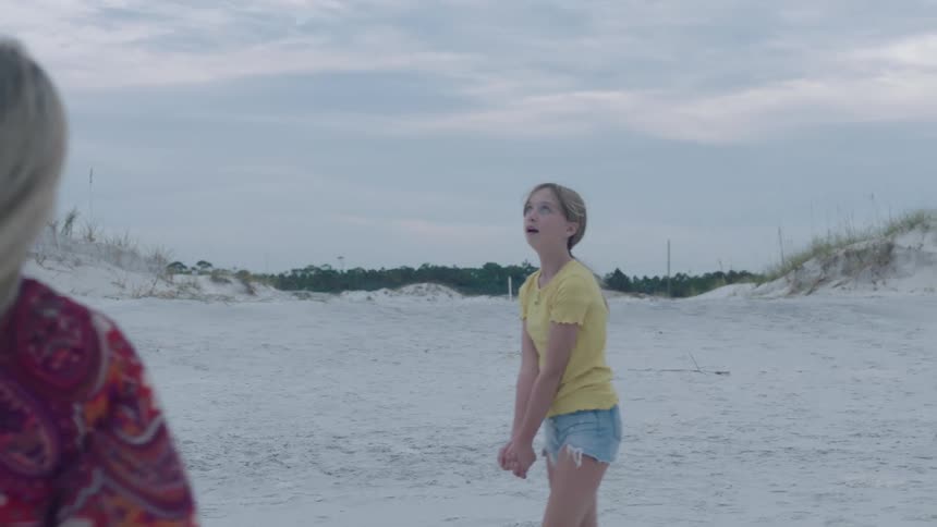 Two women playing with a ball on a beach with the sky and clouds in the background