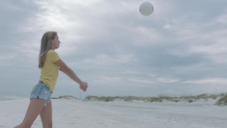 A man and two women playing with a ball on the beach with the sky and clouds in the background