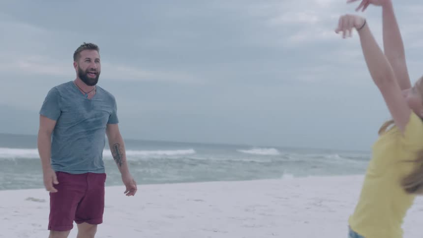 A dad hits a ball to his daughter as they play on the beach