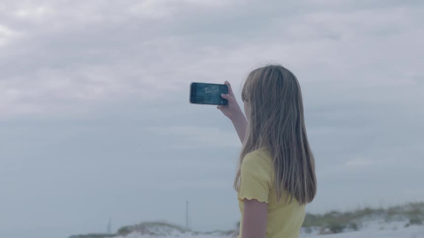 Young girl taking a picture at the beach with cell phone