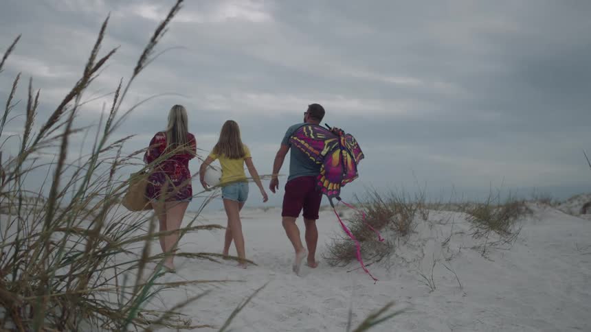Two women and a man with a kite walking on a beach with the sky and clouds in the background