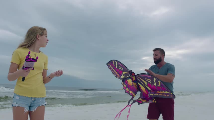 A man and a woman on a beach with a kite with the sky and clouds in the background