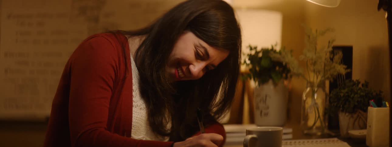 Smiling happy woman writing on a notebook with a pen over a desk in a room at home