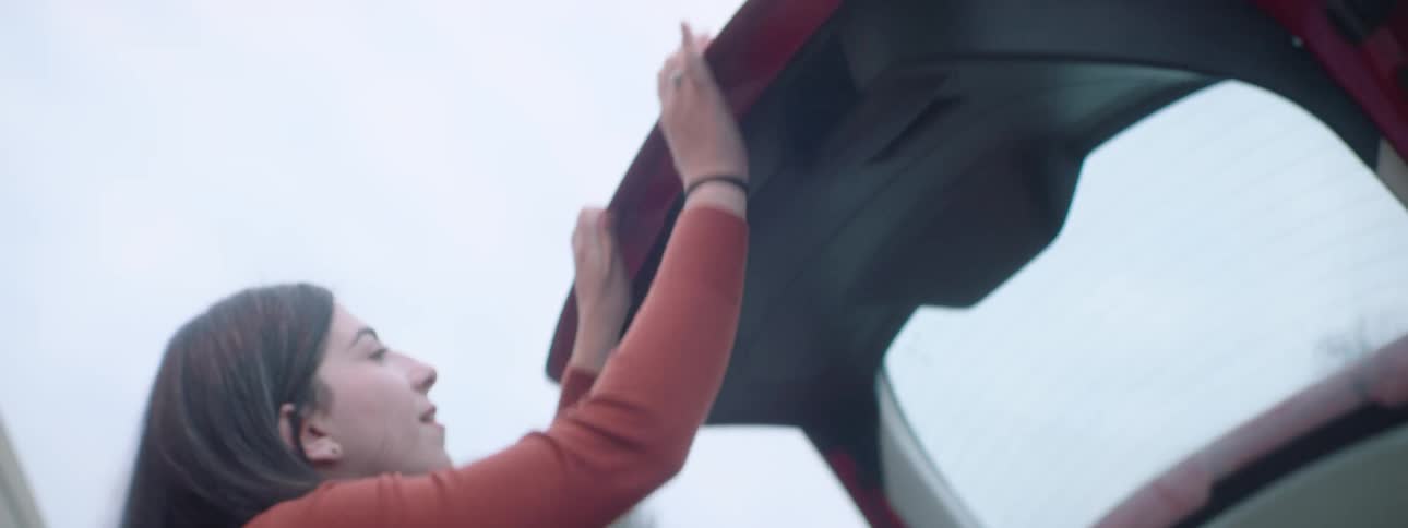 A woman walks to the driver side after loading cardboard boxes in the back of her car