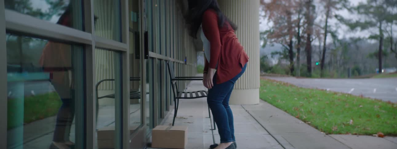 A woman with a mask placing a box in front of a building and knocking on the door
