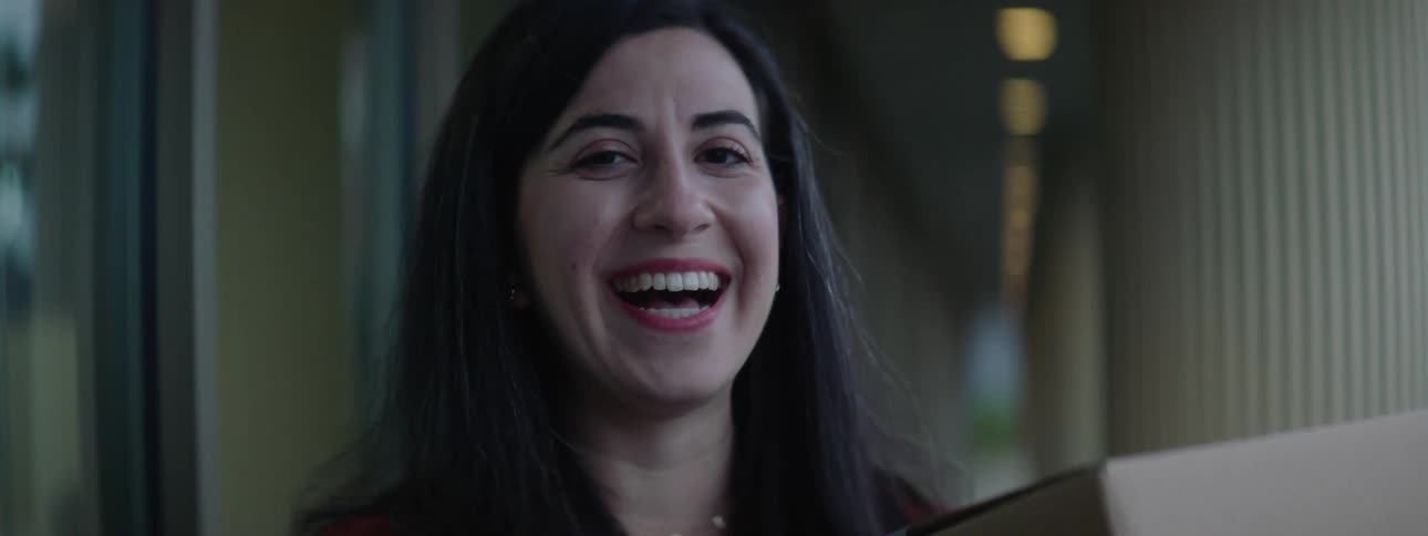 A woman standing staring and smiling while holding a box