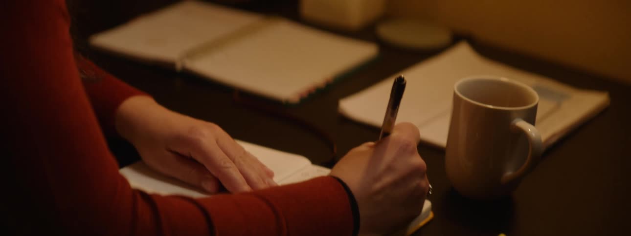 A woman sitting at a desk writing in a journal with a pen