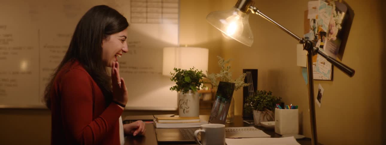 Woman greeting people on a video call through a laptop on the desk of her office