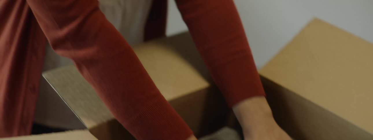 A woman in a room placing a blanket in a box with a window in the background