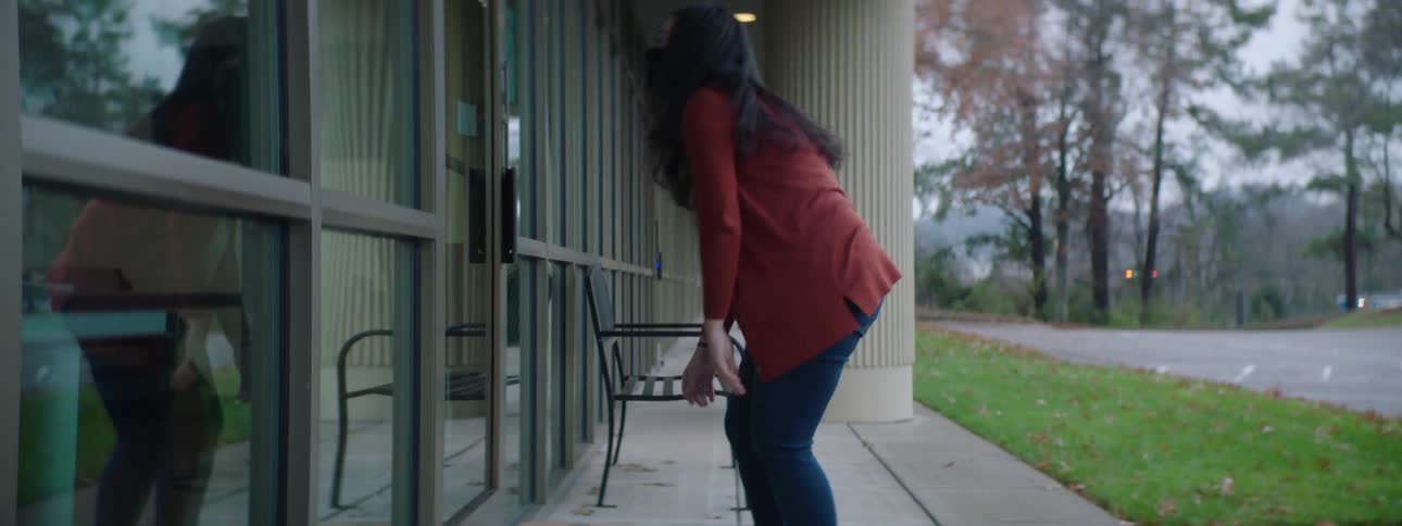 A woman wearing a mask delivers a cardboard box to a building knocks on the door and steps back