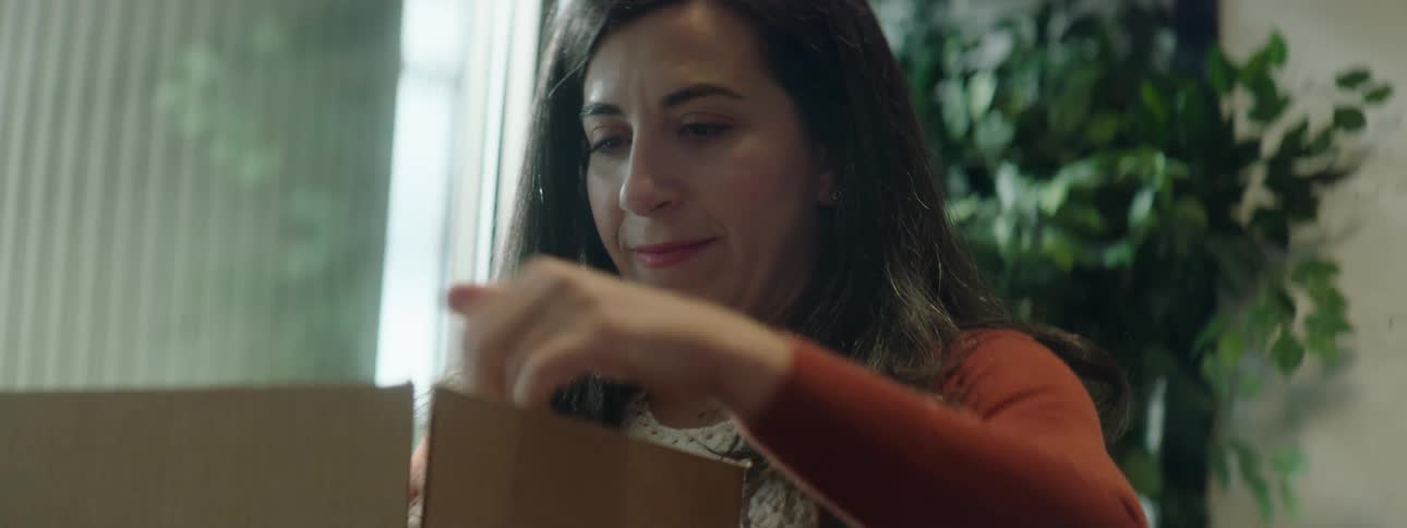 Long haired woman working in a shop assembles cardboard boxes over a table