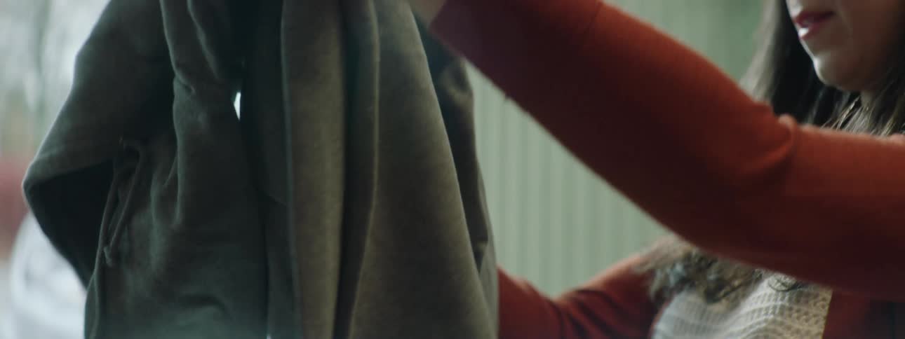 A woman at home looks at a jacket and then wipes it and blows on it