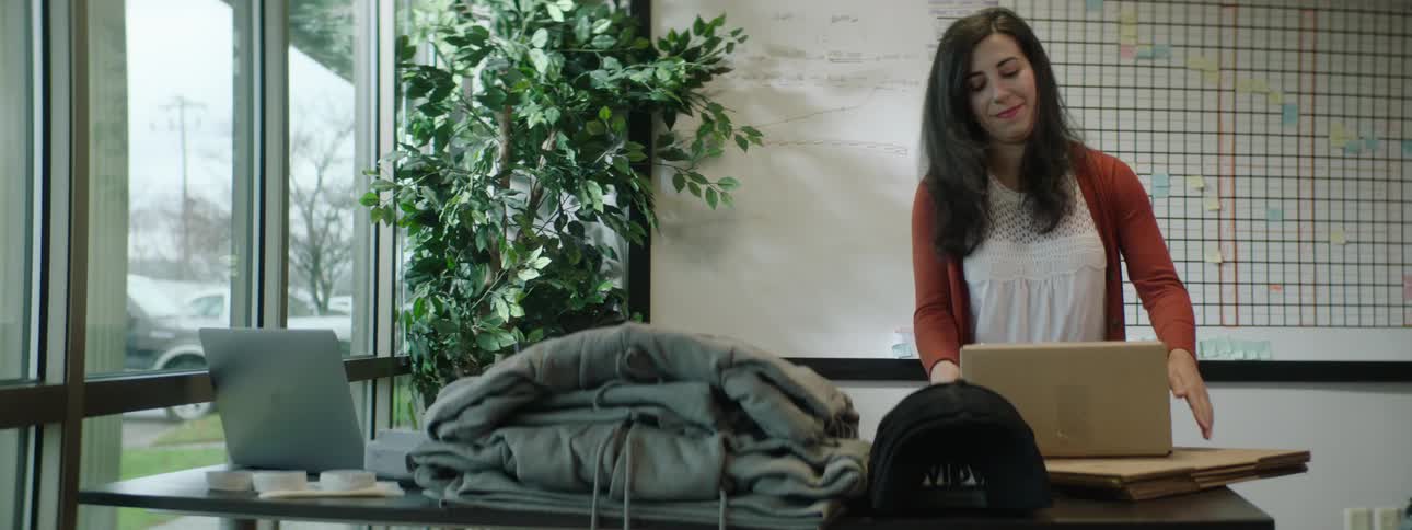 A woman tapes a box closed and carries it away