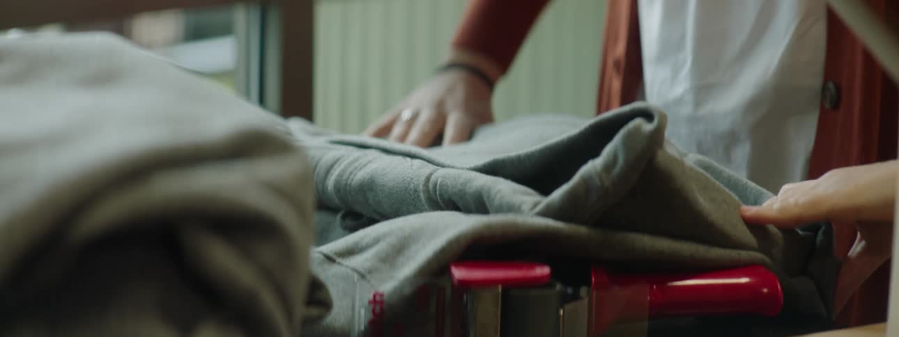 A woman smiles as she folds a sweatshirt and packs it into a cardboard box