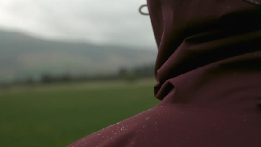 A person in a water spotted jacket walks in a field