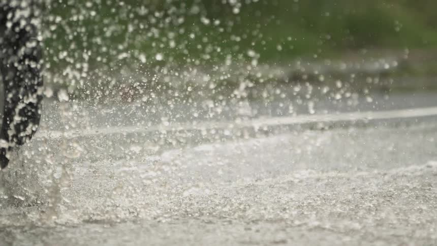 A vehicle's tire going through a puddle and sloshing water up around it as it does