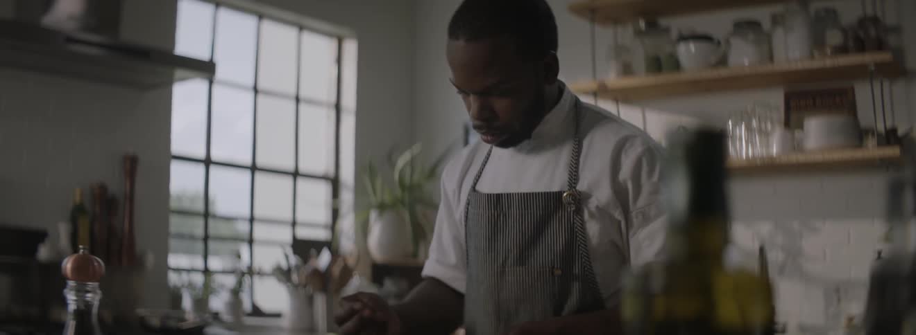 A chef works with a mandolin in a sunlit kitchen