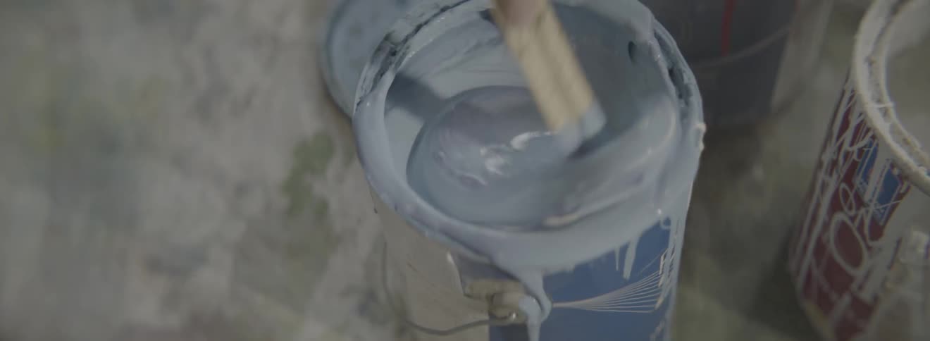 A paintbrush stirs a can of white paint
