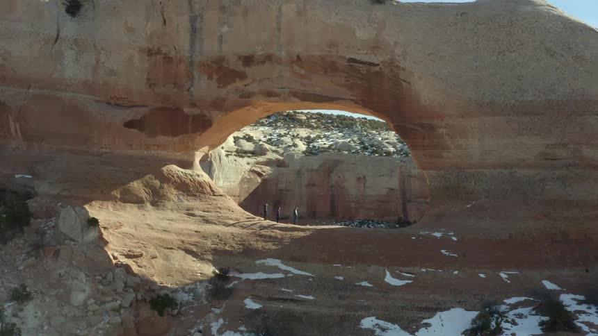 A group of people standing on a hole in the wall of a mountain in the desert