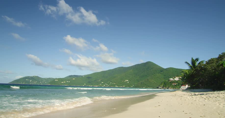 Waves rolling in on a beach with mountains in the distance and a few clouds in the sky