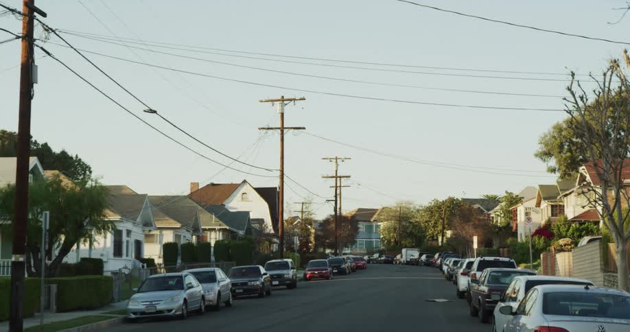A neighborhood with vehicles trees and houses with the sky and clouds in the background
