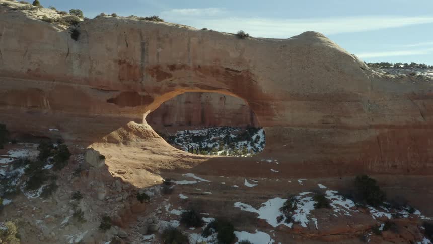 Natural arch rock formation with some snow among the plants