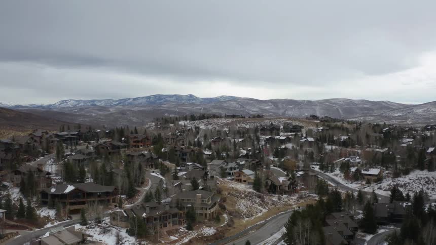 Aerial view of a neighborhood with fir trees and snow with mountains in the distance at daytime