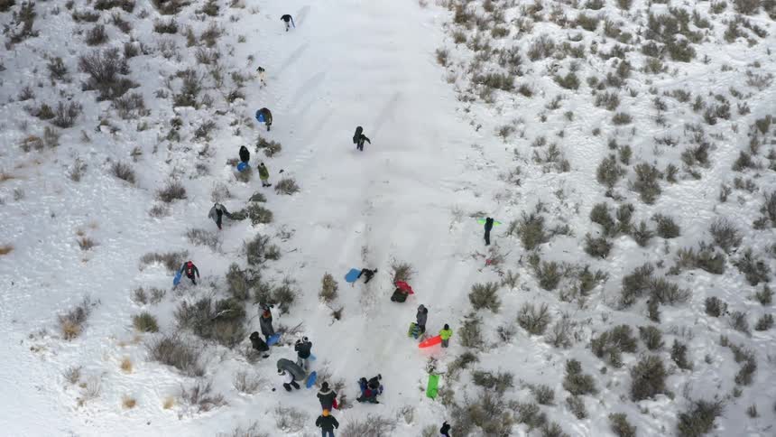 A group of people having fun riding ice slides on the side of a snow covered hill at winter